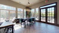 Located at 607 Villa Dr in Castle Pines, Colorado, this single-story community clubhouse offers a thoughtfully designed gathering space with a cohesive modern aesthetic throughout. The entire space is unified by striking herringbone-patterned flooring that transitions seamlessly between warm and cool tones depending on the area, adding visual depth and sophistication underfoot.

The main lounge area is bright and welcoming, featuring large multi-pane windows that flood the space with natural light and provide views of the surrounding Colorado landscape. Comfortable swivel chairs and a gold-accented coffee table create an inviting seating arrangement, while circular wall art and teal drapery add curated style.

A dedicated dining area showcases expansive floor-to-ceiling windows and French doors opening to an outdoor patio. A bold industrial-style pendant chandelier with Edison bulbs hangs above a dark high-top table surrounded by teal upholstered chairs, making it ideal for gatherings.

The kitchenette is well-appointed with dark wood cabinetry, a quartz-topped island, a stainless steel beverage refrigerator, a sink, and a decorative tile backsplash with a wall-mounted television. A cozy nook features built-in banquette seating with patterned upholstery and café-style tables, completing this versatile and stylishly appointed community space.