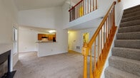 Located at 9901 Gable Ridge Terrace in Rockville, Maryland, this two-story residence offers a well-designed layout with a warm, functional interior across both levels. The main floor centers on a dramatic living area distinguished by soaring vaulted ceilings and abundant natural light streaming through multiple windows. A classic wood-banister staircase rises from the living room to the upper level, with an open balcony railing overlooking the space below. A fireplace with a clean black surround anchors one wall of the living area, adding character and comfort. The kitchen features warm honey-toned cabinetry, black appliances including a gas range and refrigerator, a double sink, and light hardwood flooring. A pass-through breakfast bar connects the kitchen seamlessly to the living area. The upper level hosts generously sized carpeted bedrooms, including a primary suite with an adjoining vanity area. Vaulted ceilings continue upstairs, enhancing the sense of space. A full bathroom on the upper level includes a single-sink oak vanity, white tile tub-shower combination, and light hardwood flooring. The upper hallway features an open balcony overlooking the main floor and provides access to a closet with a built-in rod. Neutral carpet and white walls throughout create a clean, move-in ready canvas.