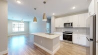 This well-appointed 2-bedroom, 2-bathroom residence offers a thoughtfully designed single-floor layout with modern finishes throughout. The open-concept kitchen and living area serves as the heart of the home, anchored by a central island with a granite countertop and an integrated sink, illuminated by a pair of stylish brass pendant lights. The kitchen is equipped with stainless steel appliances, including a range and microwave, complemented by crisp white cabinetry with subway tile backsplash. Wood-look flooring flows seamlessly through the main living areas, enhancing the bright, airy atmosphere created by neutral light gray walls and recessed lighting. A ceiling fan is featured in the living area, adding both function and comfort. The primary bedroom is a generously sized retreat with plush carpeting, a dedicated closet, and direct access to its private bathroom. The primary bath features a granite-topped vanity with white cabinetry, wood-look flooring, and a tub-shower combination. The second bedroom also offers carpeted flooring, a window with natural light, and access to the second full bathroom, which mirrors the same quality finishes. Each bedroom includes dedicated closet space. The overall design is clean, contemporary, and move-in ready.