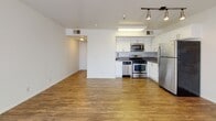 This single-floor residence is designed with a clean, contemporary aesthetic that emphasizes open living. The main living area is generously proportioned, featuring wood-look hardwood flooring that flows seamlessly throughout the space. A sliding glass door paired with a large adjacent window floods the room with natural light, while vertical blinds offer privacy control. Track lighting overhead provides focused, adjustable illumination to complement the natural light.

The kitchen is efficiently laid out and well-appointed, showcasing white shaker-style cabinetry with brushed nickel hardware, taupe quartz-style countertops, and a mosaic tile backsplash that adds visual texture. A full suite of stainless steel appliances includes a gas range, over-the-range microwave, dishwasher, and refrigerator. A skylight above the kitchen further brightens the cooking space.

The bathroom area features white cabinetry with a taupe countertop and an undermount sink, complemented by a mirrored sliding closet door nearby, maximizing both storage and the sense of space. A hallway connects the living areas to additional rooms, maintaining a logical and functional flow. Throughout the unit, crisp white walls, consistent flooring, and neutral tones create a cohesive, move-in-ready environment.