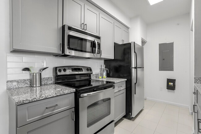 Cocina renovada con gabinetes grises, placa para salpicaduras de azulejos, pisos de baldosas y electrodomésticos de acero inoxidable. - Avalon Coconut Creek