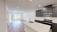 This well-designed two-bedroom, one-bathroom residence at Tamarack Circle in Skillman, NJ offers a thoughtfully planned single-floor layout. The open-concept kitchen and living area serves as the heart of the home, featuring warm hardwood-style flooring, recessed lighting, and large windows that invite natural light. The kitchen is appointed with dark charcoal shaker cabinetry, stainless steel appliances including a gas range, microwave, and refrigerator, complemented by a quartz-topped island with an undermount sink. The island provides both additional prep space and a natural connection to the living area. Both bedrooms feature plush carpeting, neutral walls, and ample natural light. The primary bedroom includes direct access to a private balcony overlooking mature trees and greenery. The full bathroom is finished with tile flooring, a tub-shower combination with decorative tile accents, a dark-cabinetry vanity, and a clean white countertop. Additional spaces include a utility room, hallways, and dedicated closet storage. The overall aesthetic is clean and contemporary throughout.