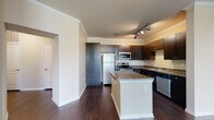 This single-floor residence offers a thoughtfully designed layout that balances comfort and functionality. The kitchen is a standout feature, showcasing rich dark cabinetry, granite-style countertops, and a full suite of stainless steel appliances including a refrigerator, electric range, and over-the-range microwave. A central island with a white base provides additional counter space and serves as a natural gathering point. Track lighting overhead adds both style and practicality to the cooking area.

Dark hardwood-style flooring extends throughout the main living areas, creating a warm, cohesive aesthetic. The living room benefits from a large window that frames a lush outdoor view, filling the space with natural light. Crown molding and a ceiling fan add classic finishing touches.

The entryway hallway features elegant panel-style doors with brushed nickel hardware, leading to the various rooms of the residence. Bedrooms are carpeted for comfort, with neutral tones throughout. One bedroom includes access to a generously sized walk-in closet outfitted with wire shelving along multiple walls for ample storage.

Two bathrooms serve the residence. One features a walk-in shower, dark vanity cabinetry with granite-style countertops, and tile flooring. The second includes a soaking tub and a wide vanity countertop, offering a relaxing retreat.