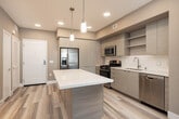 This single-floor residence at 1800 E Gene Autry Way in Anaheim, CA offers a thoughtfully designed living space with a modern aesthetic throughout. The open-concept living and kitchen area features warm wood-look flooring, recessed lighting, and a seamless flow between spaces. The contemporary kitchen is well-appointed with flat-front cabinetry in a light wood finish, stainless steel appliances including a gas range, built-in microwave, side-by-side refrigerator, and dishwasher. A white subway tile backsplash, pendant lighting, and open shelving complete the kitchen's clean, modern look. The bedrooms feature plush carpeting, ceiling fans, and windows that bring in natural light with views of the surrounding area. The primary bathroom offers a dual-sink vanity with white countertops, wood-toned cabinetry, and a separate tub and shower combination. A secondary bathroom provides similar finishes with a single vanity and walk-in closet access. Additional storage is available via dedicated walk-in closets with built-in rods and shelving. Neutral warm-toned walls and consistent wood-look flooring in common areas tie the entire residence together cohesively.