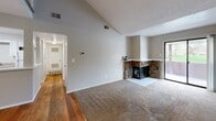This single-floor property features a striking architectural design defined by dramatically vaulted ceilings that create an expansive sense of volume in the main living area. The living room serves as the central gathering space, showcasing a corner stone fireplace with a classic hearth surround and direct access to an outdoor area via a sliding glass door, allowing natural light to filter into the room. The flooring transitions between warm hardwood and plush carpet, clearly delineating the different functional zones.

The kitchen is designed with an open-concept pass-through layout, featuring white cabinetry, granite-toned countertops, a stainless steel double sink, and white appliances including a dishwasher. Upper and lower cabinets provide ample storage throughout.

A hallway connects the main living area to additional rooms, including carpeted bedrooms equipped with ceiling fans and windows that admit natural light. Closet space is integrated into the bedrooms for practical storage.

A standout feature is the upper loft space, accessed via a staircase with decorative iron railings. This area has its own vaulted ceiling, ceiling fan, and a closet, offering flexible use as a bedroom, office, or lounge.

The bathroom includes a tiled shower-tub combination, vanity with granite-style countertop, and a large mirror with overhead lighting. Neutral gray tones and textured ceilings are consistent throughout the space.