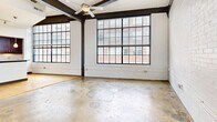 Unit 301 at 101 E. Sixth Street blends industrial character with modern finishes in the heart of downtown Winston-Salem. The open living area showcases exposed dark steel beams, whitewashed brick walls, oversized factory-style windows, and a ceiling fan, creating an airy, loft-like ambiance. The kitchen features rich dark wood cabinetry, granite countertops, stainless steel appliances, a breakfast bar, and warm hardwood flooring. Both bathrooms are finished with granite vanities, dark wood cabinetry, and tile flooring, each offering a tub/shower combo. An in-unit stacked washer and dryer adds everyday convenience to this well-appointed urban residence.