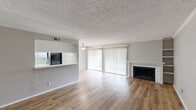 Located at 9750 Forest Ln in Dallas, TX, this single-floor, one-bedroom, one-bathroom unit offers a thoughtfully designed layout that maximizes its cozy footprint. The combined kitchen and living area forms the heart of the home, showcasing warm hardwood-style flooring, crown molding, and a textured ceiling throughout. The living room is a standout space, anchored by a wood-burning fireplace with a classic white surround and flanked by built-in shelving, perfect for display or storage. A ceiling fan and large sliding glass door with vertical blinds fill the room with natural light and provide access to an outdoor balcony area. The pass-through kitchen features white cabinetry, light countertops, a tray ceiling with overhead lighting, and a full suite of appliances including a refrigerator and range. The spacious bedroom is carpeted for comfort and includes a generous walk-in closet with built-in shelving and hanging rods. The full bathroom is clean and functional, complete with a tub-shower combination, toilet, and vanity with hardwood-style flooring. Neutral tones and a bright, open feel carry throughout the entire unit, lending a move-in-ready ambiance ideal for comfortable Dallas living.