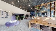 Located at 51 S Broadway in White Plains, NY, the Game Gallery & Lounge at 51 South is a generously sized single-floor entertainment and social venue designed with a sophisticated yet playful aesthetic. The space is anchored by a striking embossed tin ceiling that spans the entirety of the floor, complemented by soaring ceiling heights, recessed lighting, and globe pendant fixtures that create a warm, inviting ambiance throughout.

Upon entry, guests are welcomed by a stylish lounge area featuring plush purple velvet seating, patterned carpeting, and the prominent "51 South" branding on the wall. This transitions seamlessly into an open-concept layout with distinct zones for lounging and gaming. A refined seating area with curated furniture, a wood-paneled room divider, and large windows offering street views provides a relaxed social setting.

The gaming area is expansive and well-appointed, housing billiard tables, air hockey, foosball, skee-ball, and arcade games, all set against bold navy blue accent walls adorned with sports-themed murals. A dedicated golf simulator bay features a projection screen and artificial turf, while an indoor putting green framed by a dramatic St. Andrews course mural adds a unique, immersive touch. Open shelving, decorative greenery, and thoughtful lighting tie the entire space together cohesively.