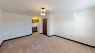 This single-floor unit offers a straightforward, functional layout with consistent dark hardwood-style flooring running throughout the main living areas, providing a cohesive and clean aesthetic. The living space is open and adequately sized, featuring neutral-toned walls, white baseboards, and a textured ceiling with flush-mount lighting that brightens the interior. A window unit air conditioner is installed in one room alongside a window fitted with blinds, allowing for natural light and ventilation. A solid entry door with a deadbolt provides secure access to the unit.

The kitchen is positioned toward the rear of the living area and is equipped with white upper cabinetry, a black refrigerator, a dishwasher, and a sink beneath upper cabinets — offering efficient use of the available space. A closet adjacent to the kitchen entry provides additional storage.

The bathroom includes a full tub-shower combo with built-in shelving, a toilet, and a vanity sink topped with a granite-style countertop. Textured walls and a mirror complete the space. Overall, the unit presents a clean, no-frills interior suited for practical, everyday living.