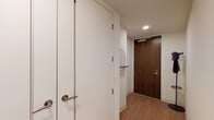 This single-floor residence is situated on a high floor, offering sweeping panoramic views of the surrounding cityscape and distant mountain ranges through expansive floor-to-ceiling windows that flood the interior with natural light throughout the day. The open-plan layout connects the kitchen, dining, and living areas seamlessly, creating a cohesive and airy living environment.

The kitchen is outfitted with light wood cabinetry extending to the ceiling, stainless steel appliances including a professional-grade range and French door refrigerator, and a central island with bar seating. Adjacent to the kitchen, a glass-wrapped dining nook provides an intimate setting framed by unobstructed city views and access to a private outdoor balcony.

The living room features large-format windows along a corner wall, delivering bright, sun-filled conditions and striking urban vistas. Light hardwood flooring runs consistently throughout the unit, enhancing the sense of continuity and warmth.

The bedrooms are generously sized, each benefiting from floor-to-ceiling windows showcasing city and hillside views. The primary bathroom is finished with light wood vanity cabinetry, a dual-sink countertop, an illuminated mirror, and a glass-enclosed shower with tile surround. The entryway is clean and functional, featuring a rich wood-toned front door and a circular accent mirror.