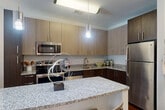 This thoughtfully designed one-bedroom, one-bathroom residence at 9300 Lottsford Rd offers a cohesive open-concept layout that maximizes every square foot. Rich hardwood flooring flows throughout the main living areas, anchoring a warm and contemporary aesthetic.

The kitchen is a standout feature, equipped with stainless steel appliances, two-tone cabinetry in light and dark wood finishes, granite countertops, and a peninsula with bar seating illuminated by pendant lighting — ideal for casual dining or entertaining.

The living room is bright and welcoming, with large windows and glass French doors that invite abundant natural light and provide direct outdoor access. The open dining area integrates seamlessly into the living space, complete with floating wall shelving.

The bedroom is a comfortable retreat, featuring plush carpet, a bold accent wall, a large window with outdoor views, and direct access to a dedicated closet. The space is generously sized to accommodate a king bed with ease.

The bathroom is finished with hardwood-style flooring, a granite-topped vanity with dark wood cabinetry, and a full tub-shower combination with a curved curtain rod. Throughout the residence, neutral wall tones, recessed lighting, and clean architectural lines create a polished, move-in-ready environment.