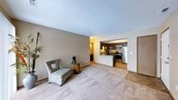 This single-floor residence offers a comfortable and functional layout designed to maximize everyday living. The spacious living area is finished with plush wall-to-wall carpeting and neutral-toned walls, creating a warm and inviting atmosphere. Large, open sightlines connect the living space to the kitchen, enhancing the sense of openness throughout.

The kitchen is a standout feature, showcasing rich dark cabinetry that contrasts beautifully with light countertops. It comes fully equipped with stainless steel appliances, including a refrigerator, microwave, and range, making it both practical and stylish. A raised breakfast bar defines the boundary between the kitchen and the living area, offering additional seating and prep space.

The textured ceiling adds a classic finishing touch throughout the unit, while the neutral color palette provides a versatile backdrop for a variety of interior styles. A doorway visible from the living area hints at additional private spaces beyond, contributing to the home's overall functional flow.

Natural and ambient lighting work together to keep the space feeling bright and welcoming. The thoughtful open-plan design, quality finishes, and well-integrated kitchen make this a highly livable and aesthetically cohesive home.
