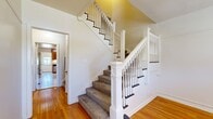 This well-appointed two-story home offers generous living space spread across two distinct floors, making it an excellent choice for large households or multi-generational living. The main floor provides the larger share of the home's footprint and welcomes residents through a dedicated entrance that flows into bright, open living areas. Polished hardwood floors run throughout the main living spaces, reflecting natural light from multiple windows and lending a warm, timeless character to every room.

The home features two kitchens, each equipped with warm oak cabinetry, stainless steel appliances including a gas range, and tile flooring—offering functional layouts ideal for everyday cooking. A dedicated laundry room with overhead cabinetry and washer/dryer hookups adds practical convenience. The three bathrooms are finished with classic tile work, warm wood vanities, and tub-shower combinations.

The upper floor houses additional bedrooms and hallways, with the generously sized primary bedroom featuring dual windows that fill the room with natural light. All five bedrooms are well-proportioned with hardwood floors and clean, neutral walls throughout. A striking staircase with white-painted spindles, a substantial newel post, and carpet treads serves as an architectural centerpiece, connecting the two floors with classic charm. Multiple hallways ensure smooth circulation throughout the home.
