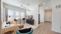 This single-story unit showcases a well-designed open-concept layout that seamlessly connects the kitchen, dining, and living areas. The living space is filled with natural light streaming through multiple large windows fitted with horizontal blinds, creating a bright and airy atmosphere. A ceiling fan overhead and recessed lighting complement the clean white walls and light wood-style flooring that runs throughout the main areas.

The kitchen is a standout feature, equipped with full stainless steel appliances including a French door refrigerator, electric range, built-in microwave, and dishwasher. Sleek gray wood-grain cabinetry extends floor to ceiling, paired with granite countertops and a white subway tile backsplash. A sliding closet door near the kitchen provides additional storage.

The living area offers generous space for both relaxing and casual dining, with room for a sofa arrangement, coffee table, and a bistro-style table with bar stools positioned near the windows. A structural column adds architectural interest to the open layout.

The bedroom features plush carpeting, triple windows for ample natural light, and enough space for a full bedroom suite. The bathroom includes wood-look tile flooring, a granite-topped vanity with wood cabinetry, and a tub-shower combination with marble-style tile surround.
