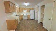Located at 6200 Dansey Dr in Raleigh, NC, this two-story home offers a practical and well-organized layout across two levels. The kitchen is a standout feature, showcasing light honey-toned wood cabinetry that extends to the upper walls, providing generous storage throughout. White appliances, including a freestanding electric range, dishwasher, and full-size refrigerator, are neatly integrated into the space. The countertops are finished in a clean, light tone that complements the cabinetry, while the wood-style flooring adds warmth and durability underfoot. Overhead flush-mount lighting keeps the kitchen bright and functional. Adjacent to the main kitchen area, a built-in open shelving unit offers additional storage or display space, adding to the home's organizational versatility. The layout flows naturally, suggesting a thoughtful floor plan designed for everyday convenience. The two-story structure provides a clear separation between living and private spaces, a common feature that adds both functionality and a sense of defined zones within the home. Overall, the space presents a clean, neutral aesthetic well-suited for comfortable day-to-day living in the Raleigh area.
