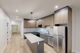 Located in the heart of downtown Calgary on 8th Avenue SW, this thoughtfully designed 2-bedroom, 2-bathroom unit offers a well-appointed single-floor layout that balances comfort and modern style. Light oak hardwood flooring runs throughout, providing a warm, cohesive feel across every room.

The kitchen is a standout feature, showcasing two-tone cabinetry with natural wood uppers and grey lower cabinets, a classic white subway tile backsplash, quartz countertops, stainless steel appliances, and a central island ideal for meal prep or casual dining. Pendant lighting adds a polished finishing touch.

The spacious primary bedroom offers generous proportions and mirrored sliding closet doors, while the second bedroom benefits from large windows that bring in natural light and city views. An additional den provides flexible space suited for a home office or guest room.

Both bathrooms are finished in a clean, contemporary style, with the vanity areas featuring grey cabinetry, quartz counters, and backlit mirrors. The unit also includes a dedicated laundry room and an abundance of closet storage throughout.

Crisp white walls, recessed lighting, and modern black hardware details contribute to the unit's clean, urban aesthetic, making it a refined and functional residence in Calgary's vibrant downtown core.
