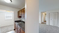 Located at 820 Carvel Dr in Dover, Delaware, this single-floor unit offers a practical and comfortable layout spread across a well-organized floor plan. The kitchen is thoughtfully appointed with warm wood-toned cabinetry, dark granite-style countertops, a stainless steel sink, and wood-look tile flooring. White appliances, including a range, microwave, and refrigerator, are neatly arranged along both walls of the galley-style kitchen, maximizing efficiency and counter space.

The living area is generously sized, featuring plush wall-to-wall carpeting and multiple windows that allow natural light to fill the room, creating a bright and welcoming atmosphere. The bedrooms continue the same carpeted flooring and are well-lit by natural light through gridded windows. One bedroom offers ample storage with two louvered double-door closets, while another features a single closet and easy hallway access.

The bathroom is clean and functional, equipped with a full tub and shower surround featuring built-in shelving, as well as a toilet and vanity. The neutral color palette throughout — crisp whites and warm beiges — lends a clean, move-in-ready feel to the entire space. A hallway connects the rooms seamlessly, contributing to the unit's practical and cohesive flow.