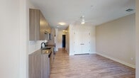 This single-floor unit features a contemporary design with a cohesive, neutral color palette and light hardwood-style flooring that runs throughout the main living areas. The open-concept layout seamlessly connects the kitchen and living space, creating a functional and airy feel.

The kitchen is outfitted with flat-front, wood-toned cabinetry extending to the ceiling for generous storage, complemented by a white subway tile backsplash and a dark quartz-style countertop. A full suite of stainless steel appliances—including a refrigerator, electric range, microwave, and dishwasher—provides modern convenience. The living area is served by a white ceiling fan and benefits from an open sightline toward the hallway and entry.

A set of white double doors in the living area provides access to a spacious closet. The bedroom features two sliding windows that allow natural light in and offer views of the surrounding community. The bathroom includes a wood-toned vanity with a gray countertop, a tub-shower combination, and light-toned tile flooring, maintaining the unit's consistent modern aesthetic throughout.