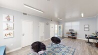 Located at 1830 Fant Dr in Fort Oglethorpe, Georgia, this single-story community amenity building offers a thoughtfully designed space built around resident comfort and shared convenience. The interior is finished with light gray walls, crown molding, and durable wood-look flooring throughout, creating a clean and welcoming atmosphere brightened by overhead fluorescent lighting.

The main lounge and activity area serves as the heart of the facility, combining casual seating with functional workspaces. Plush saucer chairs arranged atop a vibrant patterned area rug provide a comfortable gathering spot, while multiple desks equipped with computers offer dedicated stations for work or study. The room doubles as an entertainment hub, featuring a wall-mounted flat-screen television, a "Game Zone" display, and a large whiteboard, making it well-suited for both leisure and group activities.

Directly accessible via a glass-paned door, the spacious laundry facility is fully equipped with a generous number of front-loading and top-loading washing machines alongside stacked dryer units, accommodating high-volume use with ease. The room features concrete flooring and bright overhead lighting for a practical, no-frills environment.

Together, these amenity spaces reflect a functional and community-oriented design that supports the everyday needs of residents.