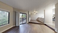 This single-floor residence offers a clean, modern aesthetic with a thoughtfully designed open layout. The main living area is anchored by durable wood-look flooring and features a ceiling fan, a textured ceiling, and a sliding glass door that opens to a private deck with views of surrounding greenery — filling the space with natural light. A raised step separates the living and dining zones, adding architectural interest while maintaining an open, connected feel. A pass-through counter links the living area directly to the kitchen, which is well-equipped with white shaker cabinetry, light countertops, a stainless steel sink, a dishwasher, and stainless appliances including a refrigerator and electric range. The bedrooms feature plush carpeting, large windows that invite natural light and outdoor views, and neutral walls that lend a calm, versatile atmosphere. The bathrooms are finished with white cabinetry, undermount sinks, light quartz-style countertops, brushed nickel fixtures, and a full tub-shower combination. Throughout the space, a consistent neutral color palette, crisp white trim, and updated finishes create a cohesive and move-in-ready environment.