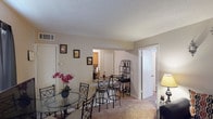 This single-floor residence offers a practical and comfortable layout across several well-defined living areas. The living room provides a cozy gathering space with plush carpet flooring, a textured ceiling, and room for a large sectional sofa and entertainment setup, with the front entry door conveniently located nearby. Adjacent to the living room, the dining area accommodates a round glass-top table with bistro-style chairs and connects seamlessly to the rest of the unit, creating an open and flowing common area. A decorative metal shelf unit adds a functional accent to the transition space between rooms. The kitchen is efficiently designed with warm oak cabinetry, ample counter space, a double-basin sink, and full appliances including an electric range, microwave, and refrigerator, all set on durable tile-style flooring. The unit includes two bedrooms, both carpeted and featuring textured ceilings. The primary bedroom is equipped with a ceiling fan, a window with natural light, and generous space for a full bedroom suite. The second bedroom also offers windows and closet storage. The bathroom includes a shower/tub combination, a vanity with storage, and tile flooring, completing this functional and well-appointed home.