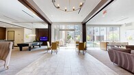 Located at 2950 Old Spanish Trail in Houston, TX, this sophisticated community amenity space offers a generously sized, single-floor layout designed for socializing and relaxation. The open-plan interior is divided into distinct yet flowing zones, beginning with a welcoming lobby entrance featuring a tufted leather sofa, elegant high-back accent chairs, and travertine tile flooring beneath a branded entryway mat. Adjacent glass-walled rooms hint at additional amenity spaces, including what appears to be a fitness center.

The main lounge area showcases a striking stacked-stone accent wall paired with rich dark wood paneling, housing a wall-mounted flat-screen TV and plush sectional seating. A glass-topped coffee table and patterned area rugs anchor the space with refined texture. Flowing seamlessly from the lounge, a game and entertainment zone features a full-size billiard table beneath a contemporary pendant chandelier, complemented by a full cabinetry kitchen with stainless steel appliances and bar seating.

Floor-to-ceiling windows and sliding glass doors flood the space with natural light and open directly to an outdoor pool courtyard, creating a seamless indoor-outdoor connection. The dining area, furnished with upholstered chairs around round tables, benefits from this abundant light. Throughout, neutral tones, recessed lighting, and modern finishes combine to deliver a polished, contemporary ambiance.