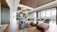 Located at 2220 Westcreek Lane in Houston's prestigious River Oaks/Galleria corridor, this elevated living space delivers a refined, contemporary aesthetic across a single, expansive floor. The entry corridor makes an immediate statement with a sculptural textured wall installation featuring organic, wave-carved wood panels backlit in warm gold, anchored by a sleek live-edge bench — setting the tone for the thoughtful design throughout.

The main living area is defined by dramatic floor-to-ceiling glass walls that flood the interior with natural light and frame sweeping panoramic views of the Houston skyline. Dark hardwood flooring flows throughout, grounding the space with warmth and continuity. Two distinct fireplace installations serve as focal points: one clad in richly textured dark stacked stone with integrated display niches, and another set within large-format metallic wall panels, both lending visual depth and architectural interest.

A dedicated lounge zone features a live-edge communal table surrounded by deep blue velvet chairs with gold bases, suspended beneath a striking cluster of black cylindrical pendant lights — an ideal setting for gatherings. Additional seating areas are curated with leather armchairs, layered area rugs, and sculptural lighting. The space's elevated position, abundant glazing, and meticulous attention to material selection create an atmosphere of polished urban luxury.