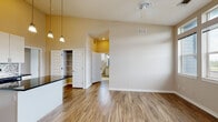 Located at 7475 32nd Avenue Pkwy in Denver, Colorado, this single-floor residence combines modern design with functional living spaces. The open-concept kitchen is a standout feature, boasting soaring ceilings with warm accent lighting, crisp white cabinetry, a decorative tile backsplash, dark stone countertops, a central island with pendant lighting, and stainless and black appliances. A built-in wine rack adds a refined touch above the upper cabinets. Wood-look flooring flows throughout the main living areas, creating a cohesive and polished aesthetic. The living area benefits from generous natural light, with a ceiling fan overhead and direct access to an outdoor space. Bedroom areas are carpeted for comfort, with one room showcasing a dramatic corner window installation that draws in abundant natural light and provides outdoor views of the surrounding greenery. Built-in open shelving in the bedroom areas offers practical storage solutions. The bathroom is finished with tile flooring, a tiled tub-shower surround, a vanity with stone countertops, and a bright window. A walk-in pantry and additional storage spaces add everyday convenience. Neutral tones throughout lend the space a clean, inviting ambiance suited for comfortable Denver living.
