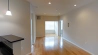 This single-floor space offers a clean, modern aesthetic defined by its open and airy layout. The interior is anchored by polished hardwood flooring that stretches throughout, reflecting both natural and artificial light to create a warm, inviting atmosphere. Recessed ceiling lights are evenly distributed across the space, providing consistent and well-balanced illumination throughout the day and evening.

The open-concept design allows for a seamless flow between living areas, making the space feel expansive and versatile. A large window at the far end of the main living area floods the interior with natural light, enhancing the bright, neutral color palette of the walls and contributing to the overall sense of openness.

The walls are finished in a soft, neutral tone that complements the light hardwood floors, creating a cohesive and understated visual harmony. Clean white baseboards frame the perimeter of each room, adding a crisp, finished detail to the design. The layout also includes a separate doorway that leads to an additional area, offering functional separation within the open floor plan. Overall, this space combines practical design with a light-filled, modern ambiance suitable for a variety of uses.