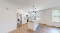 This well-appointed 2-bedroom, 2-bathroom residence offers a thoughtfully designed single-floor layout that balances comfort and modern style. The open-concept kitchen and living area serves as the heart of the home, featuring white shaker cabinetry, stainless steel appliances, a subway tile backsplash, and a central island with a built-in sink and quartz countertop, illuminated by stylish pendant lighting. Light wood-look flooring runs throughout the main living areas, complementing the bright, neutral palette. The spacious living room is bathed in natural light from large windows and a glass door leading to a balcony, and is finished with a ceiling fan overhead. A built-in counter area provides additional workspace or casual seating. Both bedrooms are carpeted and include ceiling fans and windows with natural light. The primary bedroom is generously sized with its own closet. The primary bathroom offers a long vanity with white cabinetry, quartz countertops, a framed mirror, and a glass-enclosed walk-in shower with marble-style tile. The secondary bathroom mirrors the refined aesthetic with a matching vanity and a full tub-shower combo featuring elegant marble-patterned tile surround. Two closets provide ample storage throughout the residence.