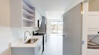 Located in Seattle's vibrant Capitol Hill neighborhood, this efficiently designed studio offers a well-planned layout that maximizes every square foot. The space features light-toned hardwood-style flooring throughout, creating a clean and cohesive aesthetic from room to room.

The galley-style kitchen is a standout feature, outfitted with stainless steel appliances including an electric range and microwave, light blue-gray cabinetry with brushed nickel hardware, white quartz countertops, a single-basin stainless steel sink, and open upper shelving for added storage versatility. The kitchen flows directly toward a large floor-to-ceiling sliding glass door that opens onto the private balcony, offering views of the surrounding Seattle cityscape and filling the living area with natural light.

The main living area is open and bright, with white walls and a built-in closet nook providing practical storage. The bathroom features wood-look tile flooring, a white vanity with clean-lined cabinetry, and a full bathtub/shower combination. A stacked washer and dryer unit is conveniently located within the bathroom, adding in-unit laundry functionality. The overall design maintains a minimalist, modern aesthetic with a neutral palette, making the space feel open and adaptable to a variety of living arrangements.