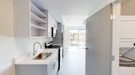 Located in Seattle's vibrant Capitol Hill neighborhood, this efficiently designed studio offers a well-planned layout that maximizes every square foot. The space features light-toned hardwood-style flooring throughout, creating a clean and cohesive aesthetic from room to room.

The galley-style kitchen is a standout feature, outfitted with stainless steel appliances including an electric range and microwave, light blue-gray cabinetry with brushed nickel hardware, white quartz countertops, a single-basin stainless steel sink, and open upper shelving for added storage versatility. The kitchen flows directly toward a large floor-to-ceiling sliding glass door that opens onto the private balcony, offering views of the surrounding Seattle cityscape and filling the living area with natural light.

The main living area is open and bright, with white walls and a built-in closet nook providing practical storage. The bathroom features wood-look tile flooring, a white vanity with clean-lined cabinetry, and a full bathtub/shower combination. A stacked washer and dryer unit is conveniently located within the bathroom, adding in-unit laundry functionality. The overall design maintains a minimalist, modern aesthetic with a neutral palette, making the space feel open and adaptable to a variety of living arrangements.