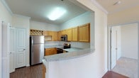Located at 1000 Applerock Dr in O'Fallon, Missouri, this single-floor residence offers a well-designed, functional layout with a variety of comfortable living spaces. The kitchen is a standout feature, equipped with stainless steel appliances including a refrigerator, electric range, over-the-range microwave, and dishwasher. Warm-toned wood cabinetry provides ample storage, complemented by light granite-style countertops and a curved breakfast bar that opens to the adjacent living and dining areas. Crown molding adds a refined architectural detail throughout the kitchen and connecting spaces. The open living and dining area is bright and welcoming, benefiting from multiple windows that invite natural light and offer views of the surrounding greenery. A pendant light fixture highlights the dining space, while hardwood-style flooring flows through the main living areas, transitioning to plush carpet in the bedrooms. The bedrooms are generously sized, each with windows for natural light; one features a ceiling fan for added comfort. The primary suite includes a vanity area with wood cabinetry and a large mirror, along with a walk-in closet with built-in shelving. Bathrooms are clean and functional, with one featuring a tub-shower combination. The overall ambiance is bright, neutral, and move-in ready.