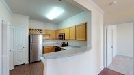 Located at 1000 Applerock Dr in O'Fallon, Missouri, this single-floor residence offers a well-designed, functional layout with a variety of comfortable living spaces. The kitchen is a standout feature, equipped with stainless steel appliances including a refrigerator, electric range, over-the-range microwave, and dishwasher. Warm-toned wood cabinetry provides ample storage, complemented by light granite-style countertops and a curved breakfast bar that opens to the adjacent living and dining areas. Crown molding adds a refined architectural detail throughout the kitchen and connecting spaces. The open living and dining area is bright and welcoming, benefiting from multiple windows that invite natural light and offer views of the surrounding greenery. A pendant light fixture highlights the dining space, while hardwood-style flooring flows through the main living areas, transitioning to plush carpet in the bedrooms. The bedrooms are generously sized, each with windows for natural light; one features a ceiling fan for added comfort. The primary suite includes a vanity area with wood cabinetry and a large mirror, along with a walk-in closet with built-in shelving. Bathrooms are clean and functional, with one featuring a tub-shower combination. The overall ambiance is bright, neutral, and move-in ready.