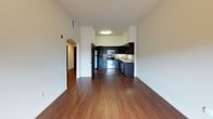 This 1-bedroom, 1-bathroom residence is designed with a cohesive, modern aesthetic across its single floor. The open-concept living area features rich hardwood-style flooring that extends throughout, creating a warm and inviting atmosphere. A ceiling fan with a light fixture adds both comfort and functionality to the main living space, which is anchored by a sliding glass door leading to a private balcony with outdoor views.

The kitchen is a standout feature, showcasing dark espresso-toned cabinetry that reaches toward the ceiling, providing generous storage. Light granite countertops offer a striking contrast against the dark cabinets, while stainless steel appliances — including a range, microwave, refrigerator, and dishwasher — complete the space with a polished, contemporary look. An arched entryway connects the kitchen to the living area, adding an architectural detail that enhances the overall flow of the unit.

The bedroom is carpeted for comfort and is bathed in natural light from a large sliding glass door that opens to a balcony. A dark-paneled interior door adds a refined design touch. The bathroom is well-finished with a dark vanity cabinet topped with granite, a vessel-style sink, elegant vanity lighting, a large mirror, and a combined shower and tub enclosure with sliding glass doors. Hardwood-style flooring continues in the bathroom, tying the space together cohesively.