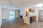 This single-story residence offers a functional and straightforward layout across several well-defined living spaces. The open living area serves as the heart of the home, featuring dark hardwood-style flooring, neutral-toned walls, and a textured ceiling throughout. A fireplace with a tiled surround anchors one wall, while a sliding glass door fills the space with natural light and provides direct access to the outdoors. Built-in shelving flanks the fireplace, adding practical storage to the living area.

The kitchen is positioned adjacent to the living space and features a peninsula with a granite-style countertop, an undermount sink, and warm wood cabinetry. A louvered door leads to a dedicated laundry or utility area, conveniently tucked between countertops. The kitchen connects seamlessly to a hallway that leads to the private areas of the home.

The bedrooms are carpeted for comfort and each include windows with blinds that allow natural light to filter in. The rooms are generously proportioned with ample wall space. The bathrooms each feature a full tub-shower combination with white tile surround, chrome fixtures, and hardwood-style flooring, maintaining a clean and consistent aesthetic throughout the home.