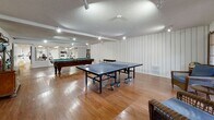Located at 23825 Anza Ave in Torrance, CA, this single-floor recreational facility at Camino Del Oro is designed to offer a well-rounded leisure and fitness experience. The space is divided into two primary zones: a generously sized game room and a dedicated fitness center, connected seamlessly to create a cohesive recreational environment.

The game room is a standout feature, showcasing warm hardwood flooring throughout and white vertical shiplap-style wall paneling that lends a clean, classic aesthetic. A full-size pool table anchors the space, complemented by a ping-pong table, providing ample entertainment options. Track lighting and recessed fixtures illuminate the room effectively, while a textured ceiling adds architectural character. Decorative round mirrors and a wooden bookcase cabinet with shelving add a touch of charm to the space.

Adjoining the game room is the fitness center, which continues the hardwood flooring and white-paneled wall design for a cohesive look. Floor-to-ceiling mirrors line the walls, enhancing the sense of openness. The room is equipped with a treadmill, weight bench, cable machine, and additional cardio and strength equipment. Bright fluorescent lighting ensures a well-lit workout environment. Together, these spaces form a comprehensive recreational facility suited for both active fitness and casual leisure.