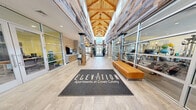 Located at 7 Crown Dr in Quincy, MA, the Elevation at Crown Colony amenity center is a generously sized, single-floor facility that blends industrial heritage with modern comfort. The dramatic entrance lobby draws immediate attention with soaring vaulted ceilings clad in reclaimed wood, exposed timber-beam trusses, and floor-to-ceiling glass that fills the space with abundant natural light. Rustic wood-wrapped columns and large-format porcelain tile flooring carry throughout, creating a cohesive and inviting aesthetic.

Adjacent to the entry, a stylish lounge area features a stone-accented fireplace wall with a mounted flat-screen TV, plush sectional and accent seating, and patterned area rugs — ideal for relaxing or socializing. A billiards area with a full-size pool table, pendant lighting, and a stone feature wall bearing the "Crown Colony Quarry" signage adds a nod to the site's local history.

The expansive fitness center is divided into two distinct zones. The cardio and strength area offers a full row of treadmills, stationary bikes, cable machines, and benches beneath recessed lighting and motivational wall graphics. A separate free weights and functional training room features dumbbell racks, adjustable benches, additional strength equipment, and a large glass garage door that opens to the outdoors, flooding the space with natural light and fresh air.