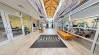 Located at 7 Crown Dr in Quincy, MA, the Elevation at Crown Colony amenity center is a generously sized, single-floor facility that blends industrial heritage with modern comfort. The dramatic entrance lobby draws immediate attention with soaring vaulted ceilings clad in reclaimed wood, exposed timber-beam trusses, and floor-to-ceiling glass that fills the space with abundant natural light. Rustic wood-wrapped columns and large-format porcelain tile flooring carry throughout, creating a cohesive and inviting aesthetic.

Adjacent to the entry, a stylish lounge area features a stone-accented fireplace wall with a mounted flat-screen TV, plush sectional and accent seating, and patterned area rugs — ideal for relaxing or socializing. A billiards area with a full-size pool table, pendant lighting, and a stone feature wall bearing the "Crown Colony Quarry" signage adds a nod to the site's local history.

The expansive fitness center is divided into two distinct zones. The cardio and strength area offers a full row of treadmills, stationary bikes, cable machines, and benches beneath recessed lighting and motivational wall graphics. A separate free weights and functional training room features dumbbell racks, adjustable benches, additional strength equipment, and a large glass garage door that opens to the outdoors, flooding the space with natural light and fresh air.
