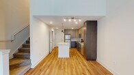 This well-appointed two-story residence offers a thoughtfully designed layout with modern finishes throughout. The main level showcases an open-concept kitchen that serves as the heart of the home, featuring two-tone cabinetry with light wood upper cabinets and darker lower cabinets, granite countertops, and a full suite of stainless steel appliances including a refrigerator, range, microwave, and dishwasher. A central island with a granite surface provides additional workspace and visual continuity, while pendant lighting and recessed track lighting illuminate the space. Warm-toned hardwood flooring extends throughout the main level, complementing the clean white walls and bright, airy atmosphere. A large sliding door with vertical blinds floods one area with natural light, and the soaring double-height ceiling adds a dramatic sense of openness. The upper level features carpeted bedrooms finished in soft neutral tones, each with ceiling fans and windows that invite natural light. A spacious walk-in closet offers generous storage with a built-in rod system. The second floor also includes an open loft-style landing area with hardwood flooring. Throughout both levels, the design balances contemporary style with functional, livable comfort.