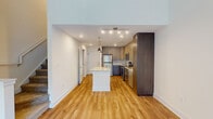 This well-appointed two-story residence offers a thoughtfully designed layout with modern finishes throughout. The main level showcases an open-concept kitchen that serves as the heart of the home, featuring two-tone cabinetry with light wood upper cabinets and darker lower cabinets, granite countertops, and a full suite of stainless steel appliances including a refrigerator, range, microwave, and dishwasher. A central island with a granite surface provides additional workspace and visual continuity, while pendant lighting and recessed track lighting illuminate the space. Warm-toned hardwood flooring extends throughout the main level, complementing the clean white walls and bright, airy atmosphere. A large sliding door with vertical blinds floods one area with natural light, and the soaring double-height ceiling adds a dramatic sense of openness. The upper level features carpeted bedrooms finished in soft neutral tones, each with ceiling fans and windows that invite natural light. A spacious walk-in closet offers generous storage with a built-in rod system. The second floor also includes an open loft-style landing area with hardwood flooring. Throughout both levels, the design balances contemporary style with functional, livable comfort.