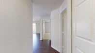This well-appointed single-floor residence offers a clean, modern aesthetic throughout, highlighted by rich dark hardwood flooring that runs through the main living areas and a neutral white and grey color palette that maximizes the sense of light and space.

The open living area is generously proportioned, featuring two windows that draw in abundant natural light alongside a sliding glass door that leads to a private balcony with views of surrounding greenery. The seamless flow between the living space and kitchen makes the layout feel open and connected.

The kitchen is designed for functionality, featuring a galley-style layout with crisp white cabinetry, sleek countertops, a stainless steel sink, and a full suite of stainless steel appliances including a gas range, microwave, dishwasher, and refrigerator. Hardwood flooring continues here, maintaining a cohesive look.

A central hallway connects the living areas to the private rooms, with convenient closet access along the way. The bedrooms offer plush wall-to-wall carpeting, ample natural light from large windows with treetop views, and a calm, restful ambiance.

The bathroom is finished in a clean, all-white palette, featuring a shower-tub combination with tiled surround and hardwood-style flooring, completing this thoughtfully designed residence.