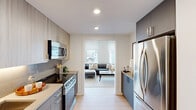 This thoughtfully designed one-bedroom, one-bathroom residence offers a compact yet functional layout spread across a single floor. The galley-style kitchen is outfitted with stainless steel appliances, including a full-size refrigerator, electric range, built-in microwave, and dishwasher. Two-toned cabinetry — combining warm wood-finish uppers with sleek gray lowers — frames dark countertops, creating a contemporary and polished aesthetic. Recessed lighting illuminates the space efficiently throughout.

The living room is bright and open, benefiting from large windows that invite abundant natural light and offer urban views of the surrounding cityscape. Light hardwood-style flooring runs continuously through the main living areas, contributing to a cohesive and airy feel. A dedicated dining nook provides additional functionality within the living space.

The bedroom features dual windows overlooking the city, allowing natural light to fill the room, and includes access to a dedicated closet. The bathroom is finished with neutral tile surrounding the shower-tub combo, complemented by clean white fixtures for a timeless look.

Overall, the residence presents a modern, minimalist design with a neutral color palette, making it a well-appointed and efficient urban living space.