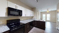 Located at 1777 Harvard Ave in College Park, Georgia, this single-floor unit offers a well-designed layout with a thoughtful blend of modern finishes and functional living spaces. The kitchen serves as a central highlight, showcasing granite countertops, dark espresso lower cabinetry paired with crisp white upper cabinets, and a full suite of black appliances including an electric range, built-in microwave, dishwasher, and refrigerator. Track lighting overhead and an L-shaped peninsula with a sink add both practicality and style. The open-concept flow from the kitchen leads into the main living area, which features wood-style plank flooring and neutral warm-toned walls that create a bright, welcoming atmosphere. A standout feature is the room with French doors that open to a private balcony, filling the space with natural light. The bedroom is carpeted for comfort and includes a ceiling fan and a window with outdoor views. The bathroom is finished with large-format tile flooring, a soaking tub with tiled surround, a dark-toned vanity, and direct access to a walk-in closet. Throughout the unit, clean lines and a neutral color palette provide a cohesive and move-in-ready aesthetic.
