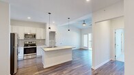Located at 1001 Sundial Cir in Sneads Ferry, NC, this single-floor, one-bedroom, one-bathroom unit offers a well-designed layout that maximizes functionality within a compact footprint. The open-concept living and kitchen area serves as the heart of the unit, where wood-look plank flooring, recessed lighting, and a ceiling fan create a clean, contemporary atmosphere. A glass-panel door leads to a private balcony, allowing natural light to fill the living space and providing outdoor views.

The kitchen is appointed with white shaker-style cabinetry extending to the ceiling, granite countertops, a geometric tile backsplash, and a full suite of stainless steel appliances. A central island with a granite top and integrated sink is illuminated by pendant lighting, offering additional workspace and a natural gathering point.

The bedroom features soft carpeting, a ceiling fan, and a window with outdoor views, providing a comfortable and well-lit retreat. A dedicated closet offers organized storage. The bathroom includes a granite-topped vanity with shaker cabinetry, a large mirror, and wood-look tile flooring. A separate laundry room accommodates a full-size washer and dryer with overhead wire shelving for additional storage.