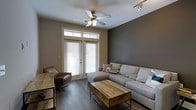 Located at 722 Island Park Dr. on Daniel Island, SC, this single-story residence offers a thoughtfully designed interior that blends comfort with contemporary style. The living area serves as the heart of the home, showcasing dark hardwood flooring that anchors the space with warmth and sophistication. A bold, deep-toned accent wall adds depth and contrast against the neutral surrounding walls, creating a modern yet inviting atmosphere. Natural light pours in through French doors fitted with transom windows above, bringing the outdoors in while providing access to the exterior. A ceiling fan with a light fixture enhances airflow and comfort, while track lighting along the ceiling offers additional illumination. The living space is generously proportioned, comfortably accommodating a large sectional sofa, a leather accent chair, and a rustic wood-and-metal coffee table that adds an industrial touch. The overall design aesthetic is cohesive and refined, blending earthy tones, natural textures, and modern furnishings to create a space that feels both stylish and livable. This Daniel Island property delivers a compelling combination of location, design, and single-level convenience.