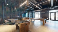 Located at 301 Winchester Ave in New Haven, CT, this single-floor recreational space showcases a striking industrial aesthetic throughout. The open-plan layout is defined by exposed ceiling ductwork and conduit painted in dark tones, complemented by sleek linear pendant lighting that illuminates the polished concrete floors below. Large steel-framed windows and glass partition walls flood the interior with natural light, offering views of the surrounding exterior while maintaining a sense of openness and connectivity.

The space is fully equipped for recreation and social engagement. A central foosball table serves as a focal point, flanked by a full-size pool table and a solid wood ping pong table with sturdy steel legs. A lounge seating area with a sofa and accent chairs provides a relaxed retreat, while a dedicated media wall featuring a wall-mounted flat-screen TV and a wood slat accent panel with bar-height seating and stools creates an ideal spot for viewing or casual gathering. A cue rack mounted to the wall keeps game equipment neatly organized.

A set of steel-framed double glass doors opens to the exterior, enhancing the flow of natural light and providing direct outdoor access. The combination of warm wood tones, dark walls, and industrial detailing gives the space a sophisticated yet inviting urban character, making it well-suited for community recreation or social events.
