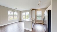 This well-appointed single-floor residence showcases a thoughtfully designed open-concept layout that seamlessly integrates the kitchen, dining, and living areas. The living space is bathed in natural light through an expansive arrangement of double-hung windows fitted with clean white blinds, offering pleasant views of surrounding greenery and the neighboring streetscape. Rich hardwood-style flooring flows throughout the main living areas, lending warmth and continuity to the space.

The kitchen is a standout feature, centered around a sleek white island with a built-in sink and light quartz countertops. It is equipped with stainless steel appliances, including a gas range, overhead microwave, dishwasher, and refrigerator. A subway tile backsplash in soft sage tones adds a refined, contemporary touch, complemented by crisp white cabinetry.

The bedrooms are generously proportioned, each carpeted for comfort and featuring windows that draw in natural light and outdoor views. The two full bathrooms maintain a consistent, clean aesthetic, with white subway tile surround tub-shower combinations, hardwood-style flooring, and chrome fixtures throughout.

Neutral warm-gray walls, recessed lighting, and clean white baseboards and trim unify the space, creating a bright, modern ambiance that is both functional and inviting.