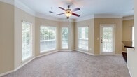 Located at 9505 Glen Forest Dr in Greenville, South Carolina, this single-floor residence offers a thoughtfully designed layout with a warm, neutral color palette throughout. The spacious living area is anchored by crown molding, plush wall-to-wall carpeting, and a ceiling fan with light fixture. A bank of large windows with slatted blinds floods the room with natural light and provides views of the surrounding greenery, while a door leads directly to an outdoor balcony or patio, extending the living space further. The kitchen features a galley-style layout with crisp white cabinetry, dark granite-style countertops, hardwood flooring, and black appliances including a refrigerator, dishwasher, and range. A louvered pantry door and ample upper and lower cabinet storage make this kitchen both practical and organized. The bedrooms are generously sized, each equipped with ceiling fans and carpeted floors. The primary bedroom includes access to a walk-in closet with wire shelving and a dedicated en-suite bathroom. The bathroom is appointed with a wide double-sink vanity topped with dark speckled countertops, mirrored medicine cabinets, and stylish vanity lighting. Throughout the home, consistent warm beige tones, white trim, and clean finishes create a cohesive and inviting atmosphere.