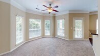 Located at 9505 Glen Forest Dr in Greenville, South Carolina, this single-floor residence offers a thoughtfully designed layout with a warm, neutral color palette throughout. The spacious living area is anchored by crown molding, plush wall-to-wall carpeting, and a ceiling fan with light fixture. A bank of large windows with slatted blinds floods the room with natural light and provides views of the surrounding greenery, while a door leads directly to an outdoor balcony or patio, extending the living space further. The kitchen features a galley-style layout with crisp white cabinetry, dark granite-style countertops, hardwood flooring, and black appliances including a refrigerator, dishwasher, and range. A louvered pantry door and ample upper and lower cabinet storage make this kitchen both practical and organized. The bedrooms are generously sized, each equipped with ceiling fans and carpeted floors. The primary bedroom includes access to a walk-in closet with wire shelving and a dedicated en-suite bathroom. The bathroom is appointed with a wide double-sink vanity topped with dark speckled countertops, mirrored medicine cabinets, and stylish vanity lighting. Throughout the home, consistent warm beige tones, white trim, and clean finishes create a cohesive and inviting atmosphere.
